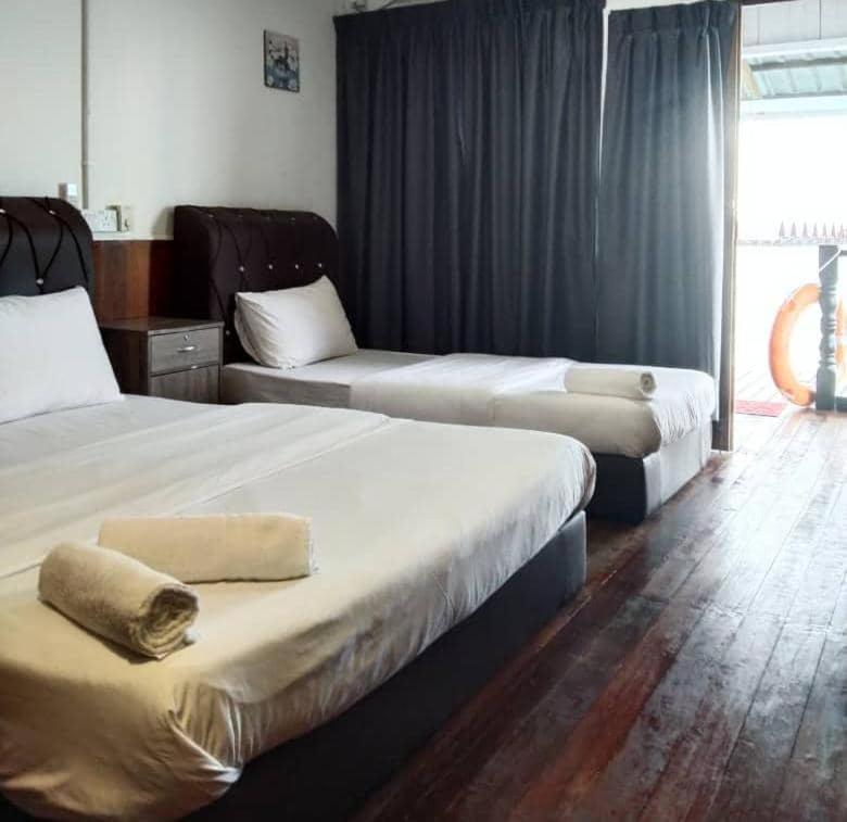 A comfortable bedroom at Sea Plus Water Chalet Resort in the Celebes Sea offering a double and single bed, direct access to the private balcony, dark hardwood floors, and a/c.
