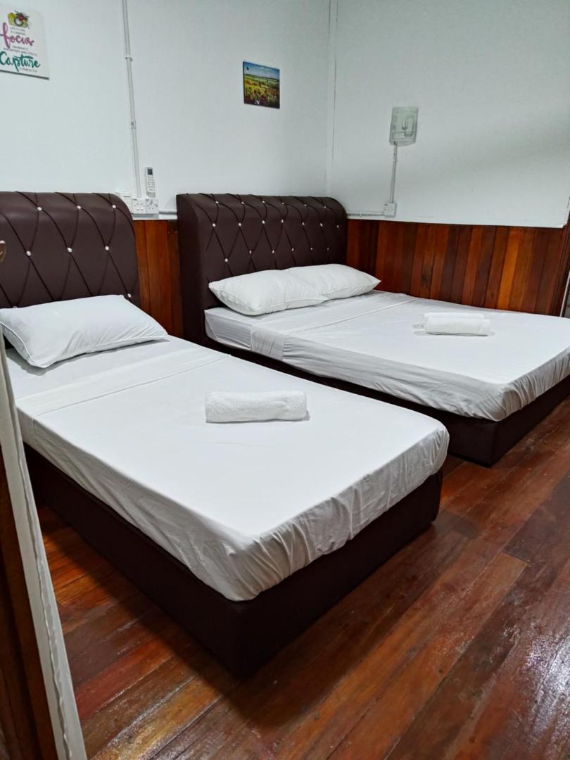A family bedroom at Sea Plus Water Chalet Resort near Semporna showcasing a double and single bed, wood-paneled walls, varnished timber floors, and air conditioning.